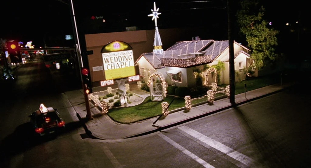 Intolerable Cruelty (2003) movie still: wide — A small wedding chapel sits on a dark street corner at night illuminated by lights. A taxi drives…