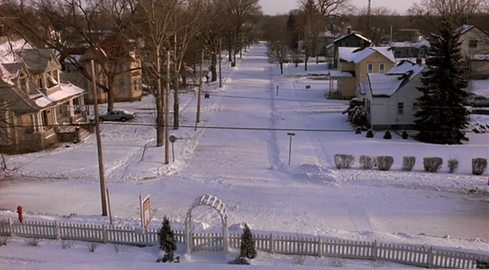 Groundhog Day (1993) movie still: establishing — A residential street in winter is covered in a thick layer of untouched snow. Single-family homes…