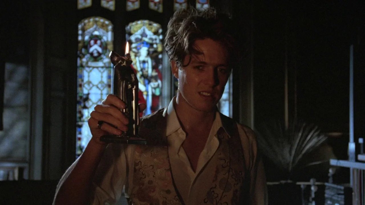 The Lair of the White Worm (1988) movie still: medium — An interior space features tall stained-glass windows in the blurred background. A young man…