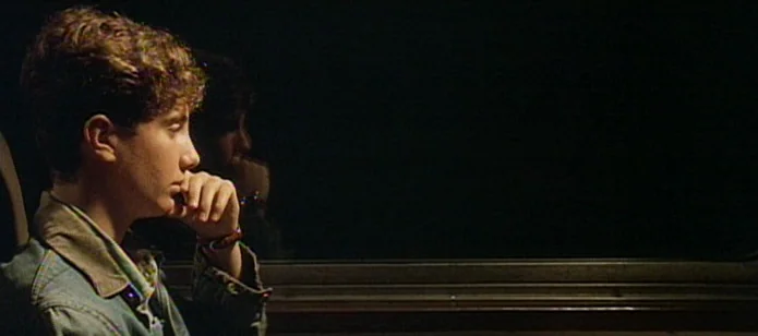 The Neon Bible (1995) movie still: medium — A teenage boy sits on a vehicle bench at night next to a window. The exterior outside the glass is…