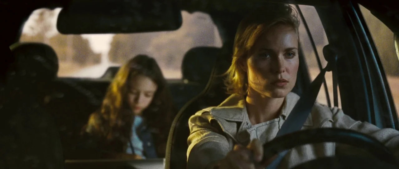Silent Hill movie still: medium — Interior of a car driving along a road during the daytime. An adult woman drives while a young child sits in the…
