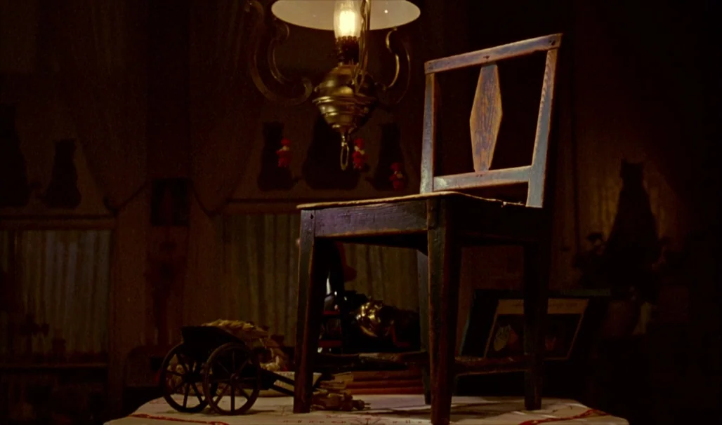 Fanny and Alexander (1982) movie still: medium — A wooden chair sits upon a covered table in a darkened, dimly lit room. Small decorative objects…