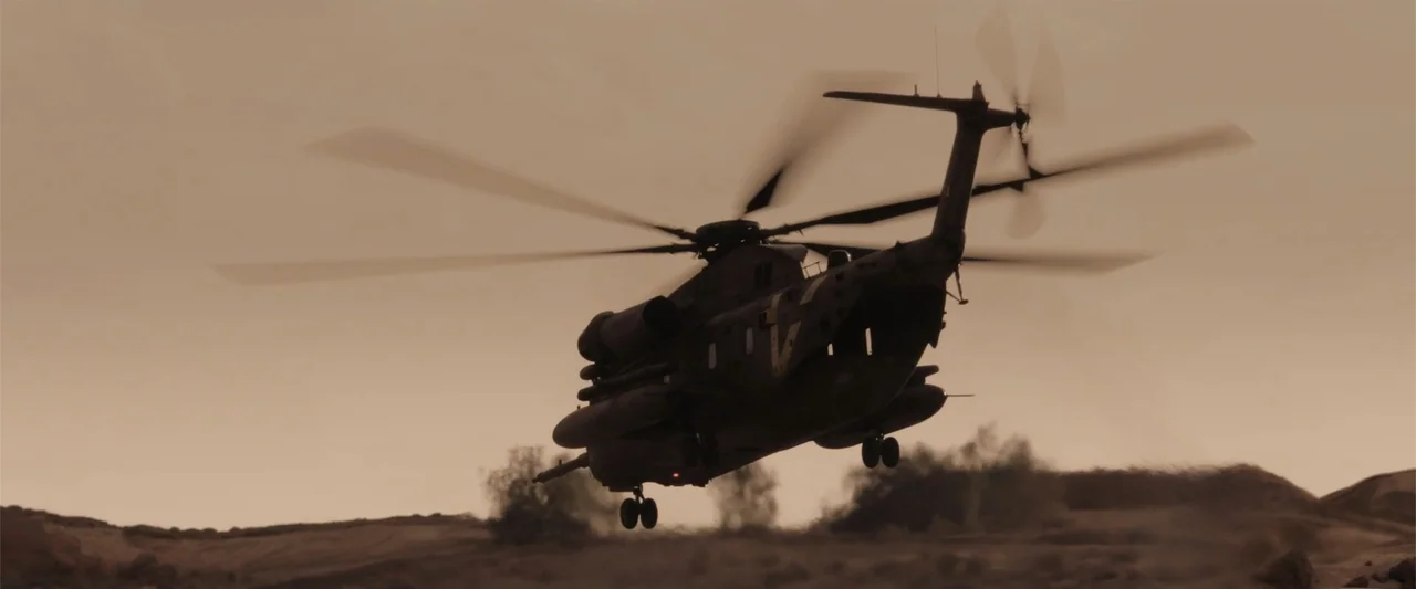 Black Site (2022) movie still: wide — A military helicopter flies at low altitude over a flat, barren, dusty desert plain. The aircraft is captured…