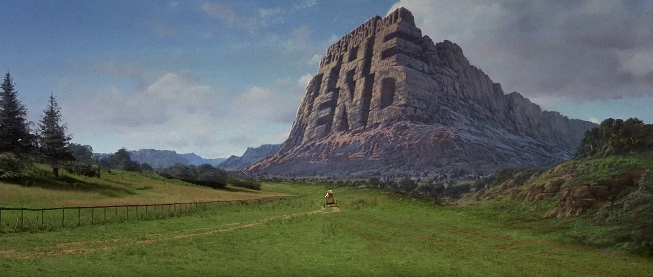 History of the World: Part 1 (1981) movie still: establishing — A vast green mountain valley features a large craggy rock formation in the distance.…