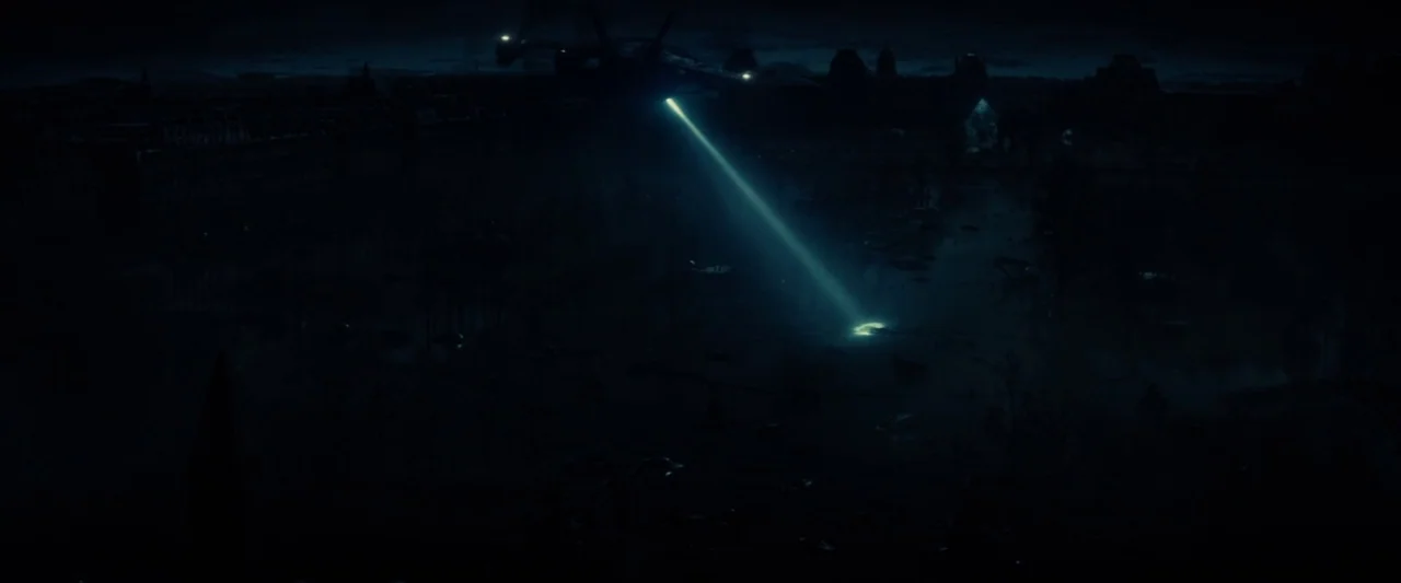 Edge of Tomorrow (2014) movie still: establishing — A dark, destroyed urban area at night shows the silhouette of a large aircraft. A sharp cyan…