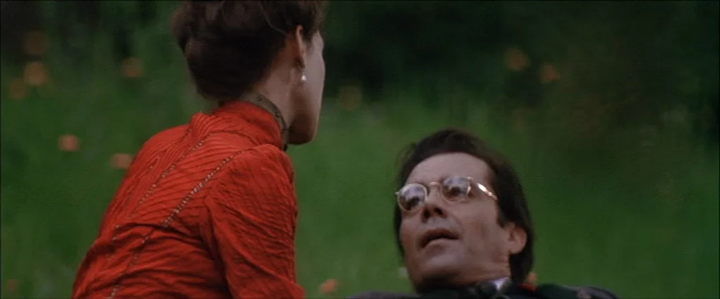 Death In Venice (1971) movie still: medium — Two people are positioned in a lush green field with scattered small orange flowers. A woman in a red…