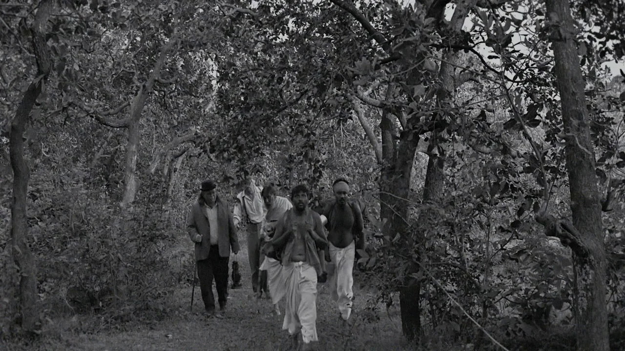 The Field Guide to Evil (2018) movie still: wide — A group of diverse men walk along a dirt trail through dense trees. The men move toward the…
