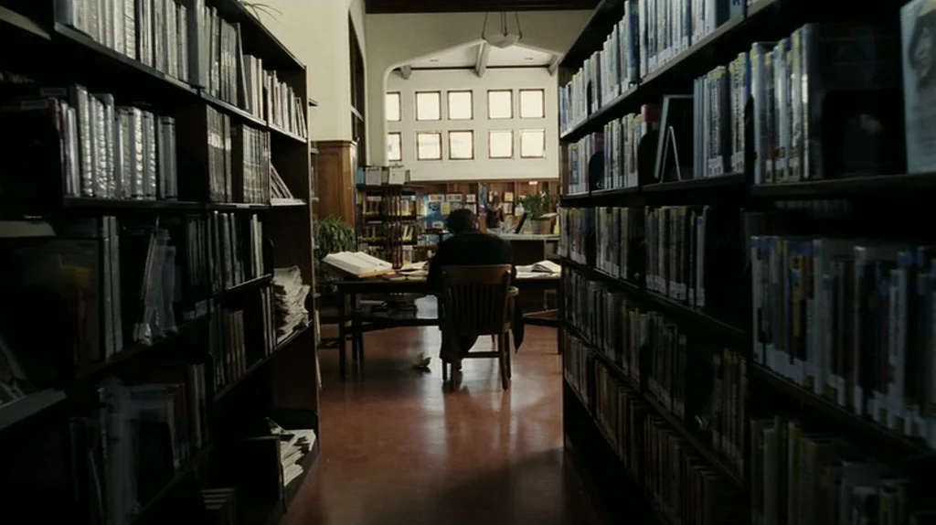 The Assassination of Richard Nixon (2004) movie still: wide — A quiet room filled with tall black shelves packed with numerous books. A person sits…