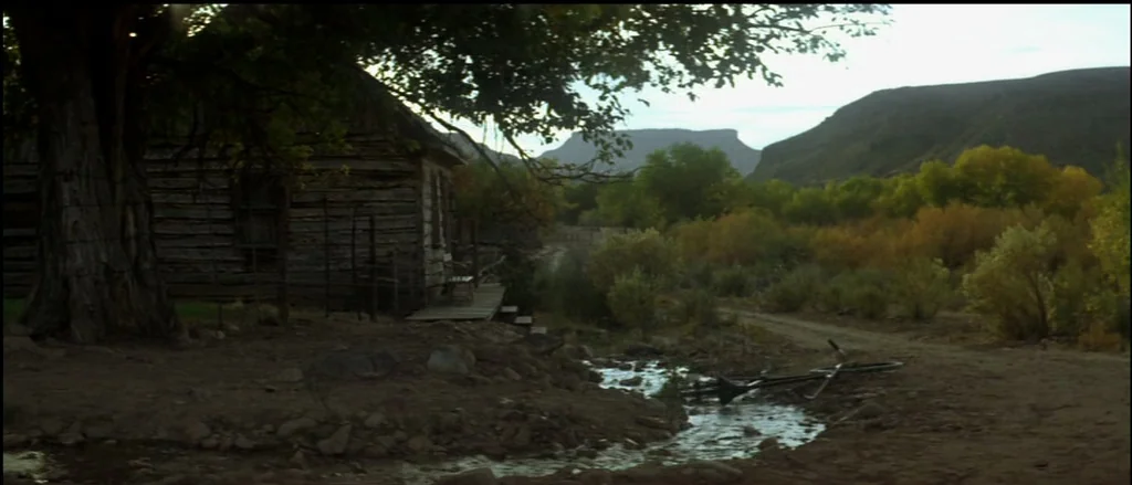 Butch Cassidy and the Sundance Kid (1969) movie still: establishing — A rustic wooden cabin sits beside a small stream in a rural valley setting. An…