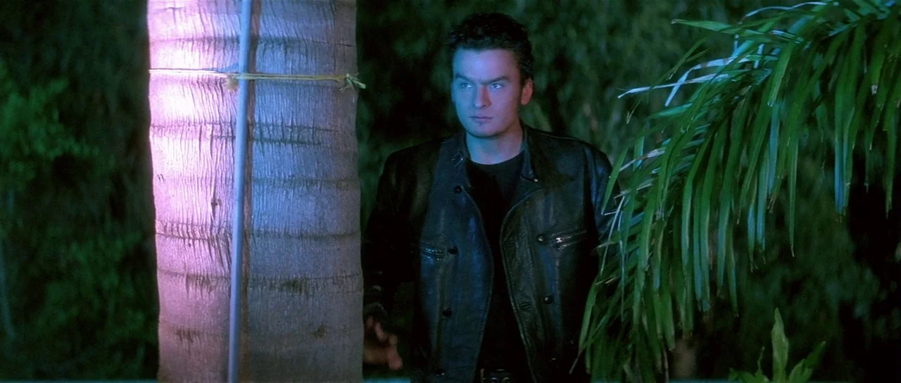 Lost Highway (1997) movie still: medium — A man stands outdoors at night between palm trees in an urban tropical setting. The man in a leather…