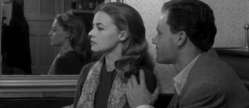 Les Amants (1958) movie still: medium — A woman looks into a wall mirror while a man stands beside her. He places his hand on her shoulder while…