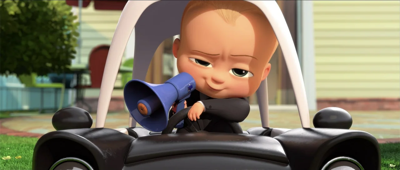 The Boss Baby (2017) movie still: medium — A cartoon baby sits in a small black toy car outdoors. The subject holds a blue megaphone while gripping…