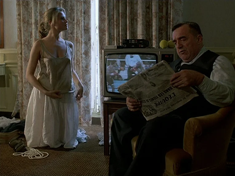 Detective (1985) movie still: fullbody — A hotel room with patterned curtains and wall-to-wall carpeting. A woman kneels on the floor while an older…