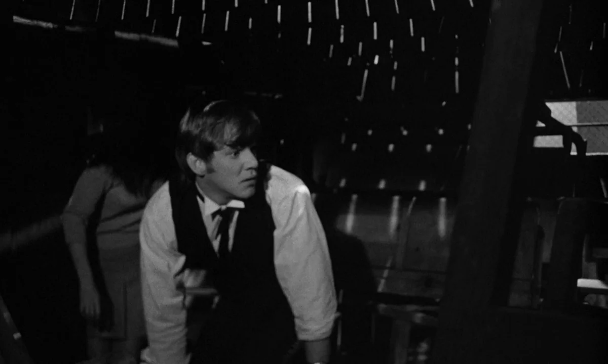If…. (1968) movie still: medium — An attic interior with dark wooden slats creating a striped pattern on the floor. A man in a vest crouches while…
