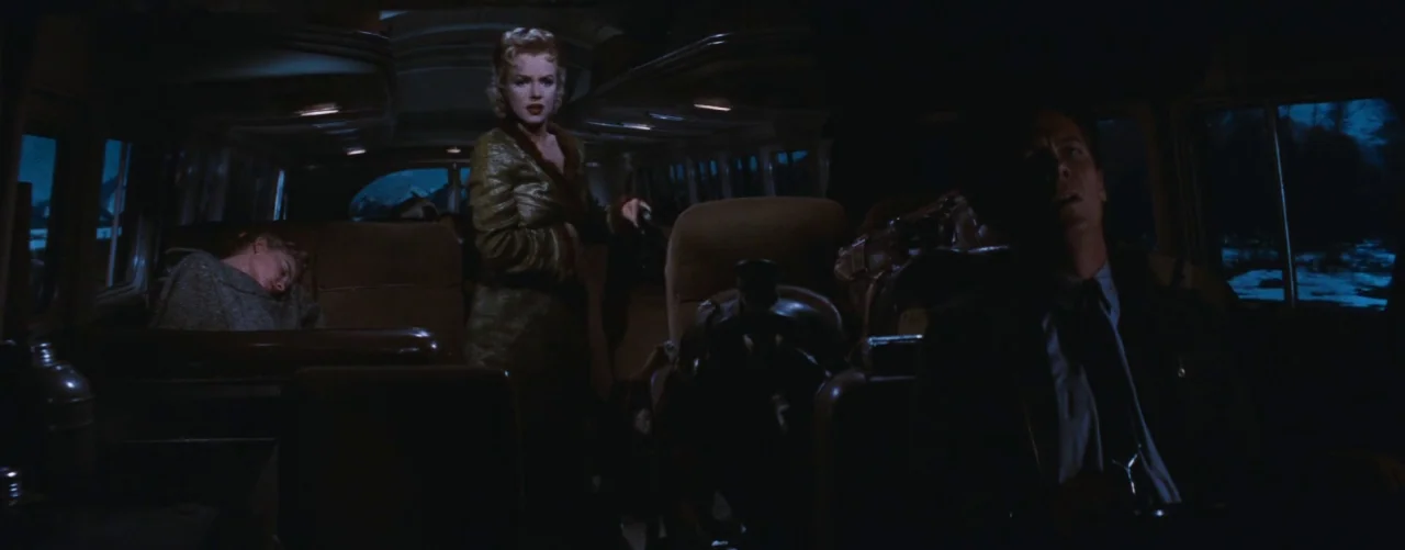 Bus Stop (1956) movie still: wide — The dimly lit interior of a night bus shows passengers in vintage 1950s attire. A woman stands in the aisle…
