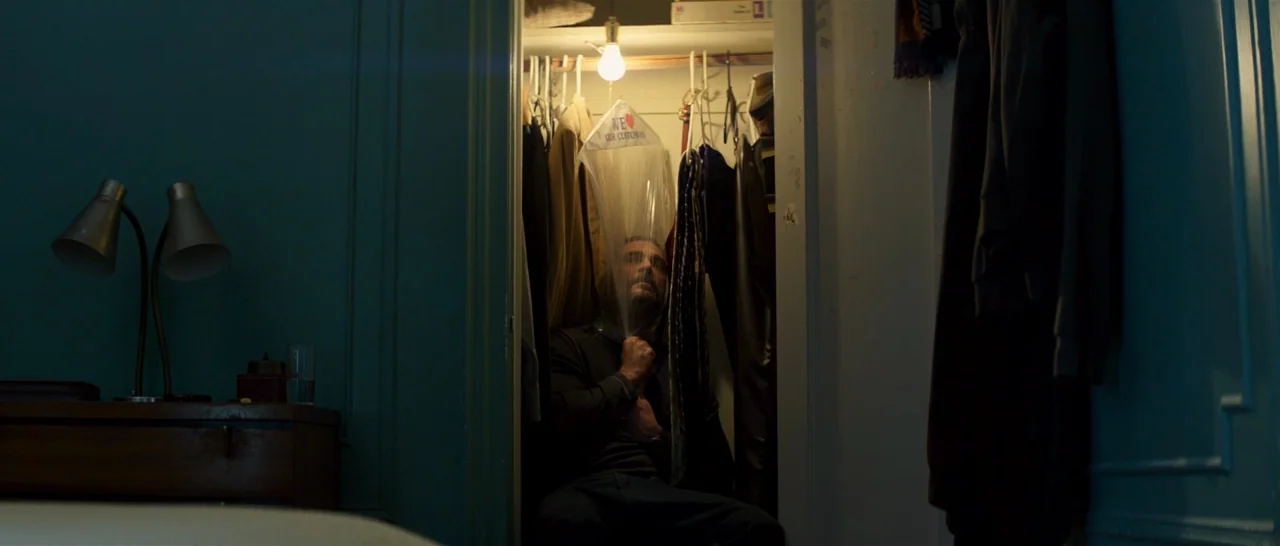 You Were Never Really Here (2017) movie still: wide — A man sits inside a cramped closet filled with hanging coats and clothing items. He pulls a…