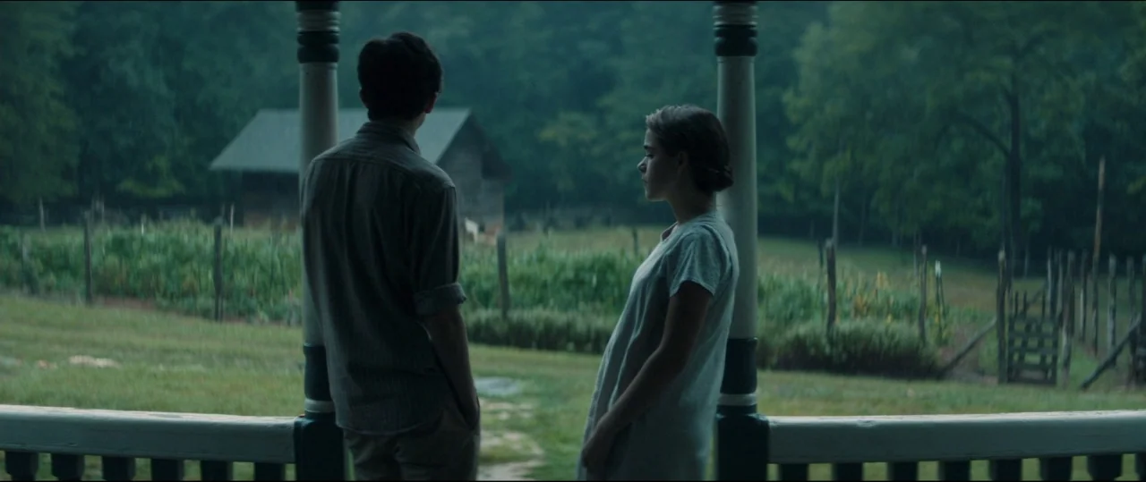 One & Two (2015) movie still: fullbody — A rural wooden porch overlooks a green field with a distant barn during rain. A young couple stands near…