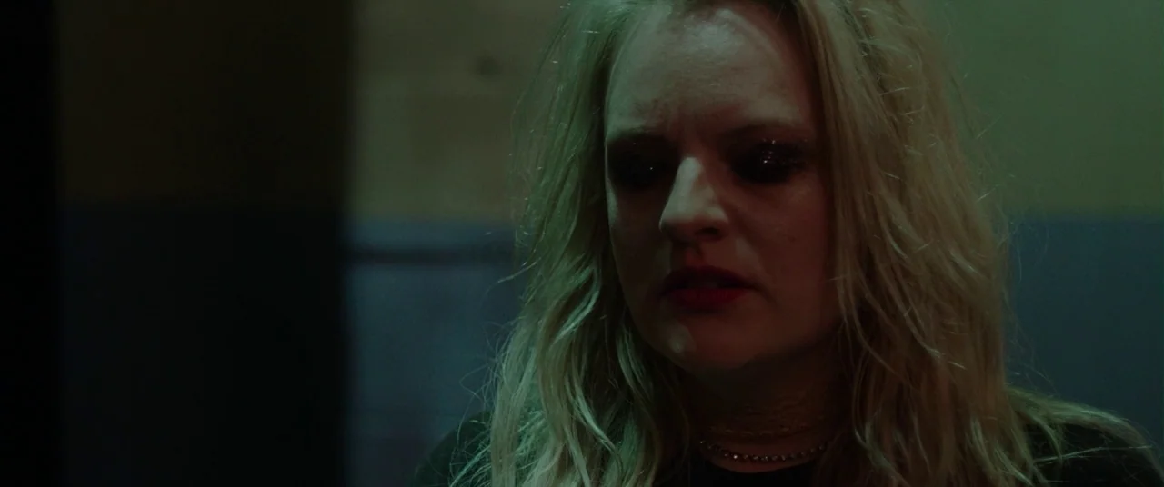 Her Smell (2018) movie still: closeup — A dimly lit room with a dark wall provides a stark, minimalist backdrop. A blonde woman with glittery eye…