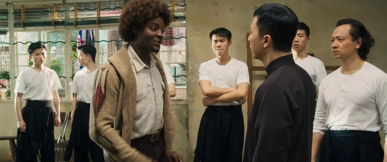 Ip Man 4: The Finale (2019) movie still: medium — A group of men in traditional martial arts uniforms stand in a brightly lit room. A man in a knit…