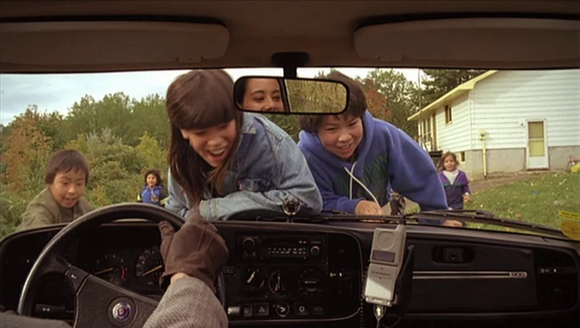 Dance Me Outside (1994) movie still: medium — A group of children stand around the front of a stationary Saab automobile. The children look down…