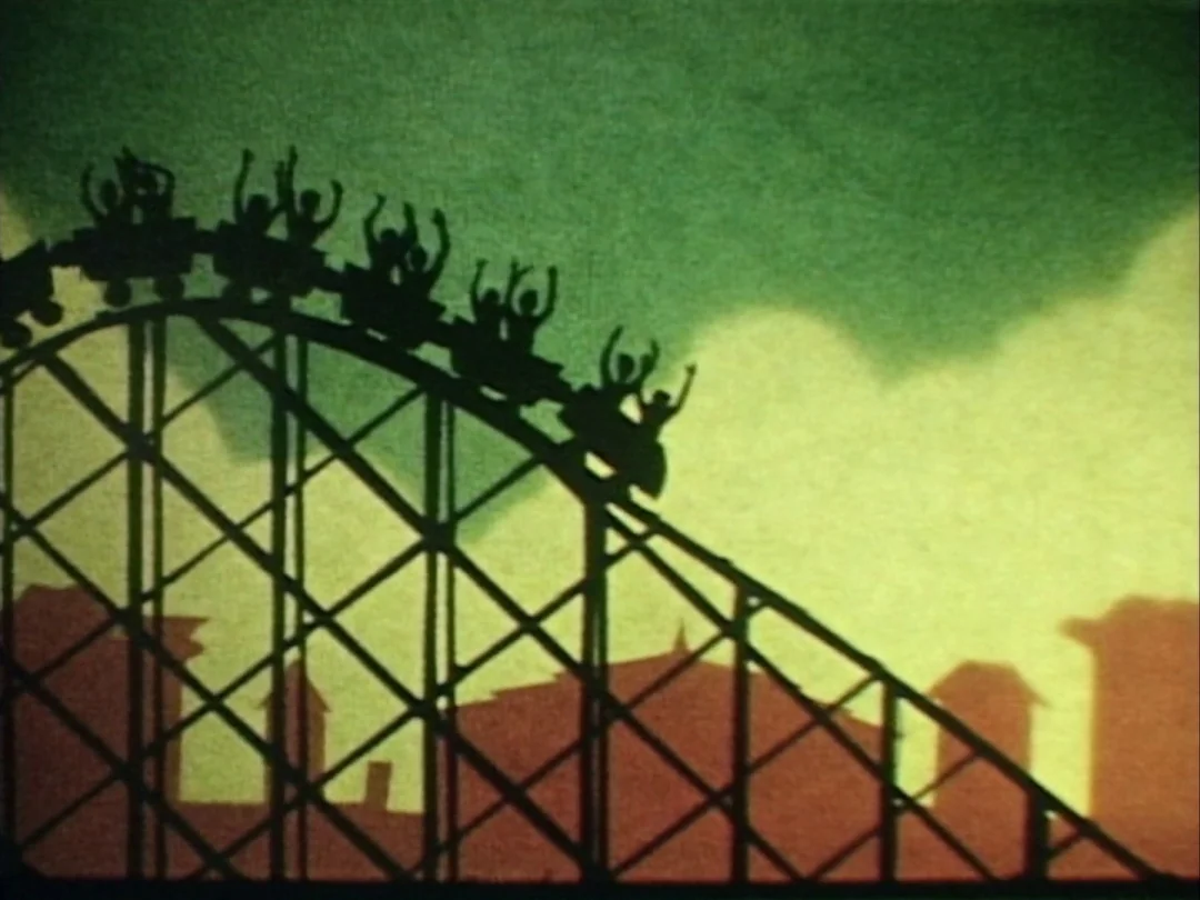 My Winnipeg (2007) movie still: wide — A 2D animated amusement park setting featuring a wooden roller coaster against a backdrop. Passengers in the…