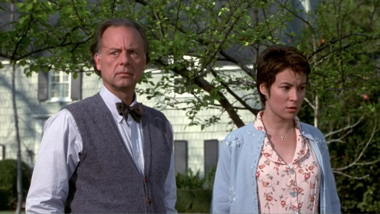 Music from Another Room (1998) movie still: medium — A man and a woman stand outdoors in front of a shingled suburban house. The two individuals…