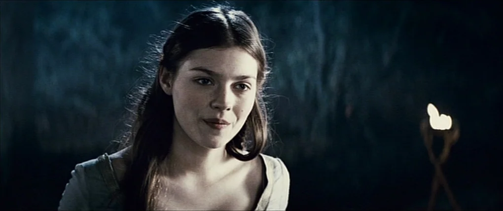Your Highness (2011) movie still: closeup — A woman stands within a dark, rocky enclosure with indistinct stone walls. A lone torch sits in the…