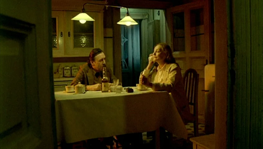 Almanac of Fall (1984) movie still: medium — A dimly lit room with a dining table placed centrally under two pendant lights. A man and woman sit…