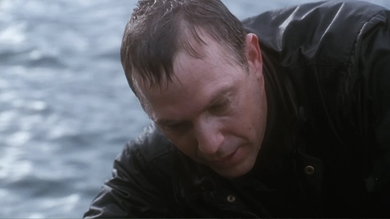 The Bodyguard (1992) movie still: closeup — An outdoor waterfront setting features a man leaning over a body of water. The man stares down towards…