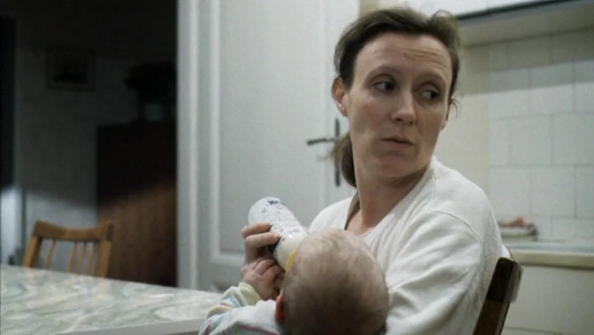71 Fragments of a Chronology of Chance (1994) movie still: medium — A domestic kitchen space contains a table and cupboards against a tiled wall. A…