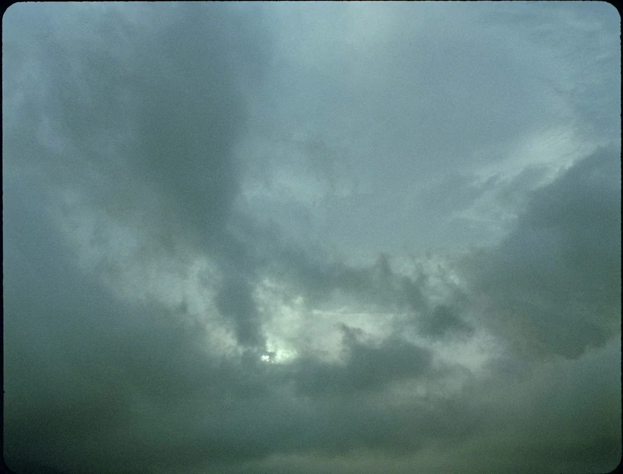 Godland (2022) movie still: establishing — A dense expanse of overcast clouds fills the entire frame from edge to edge. Subtle variations in shadow…