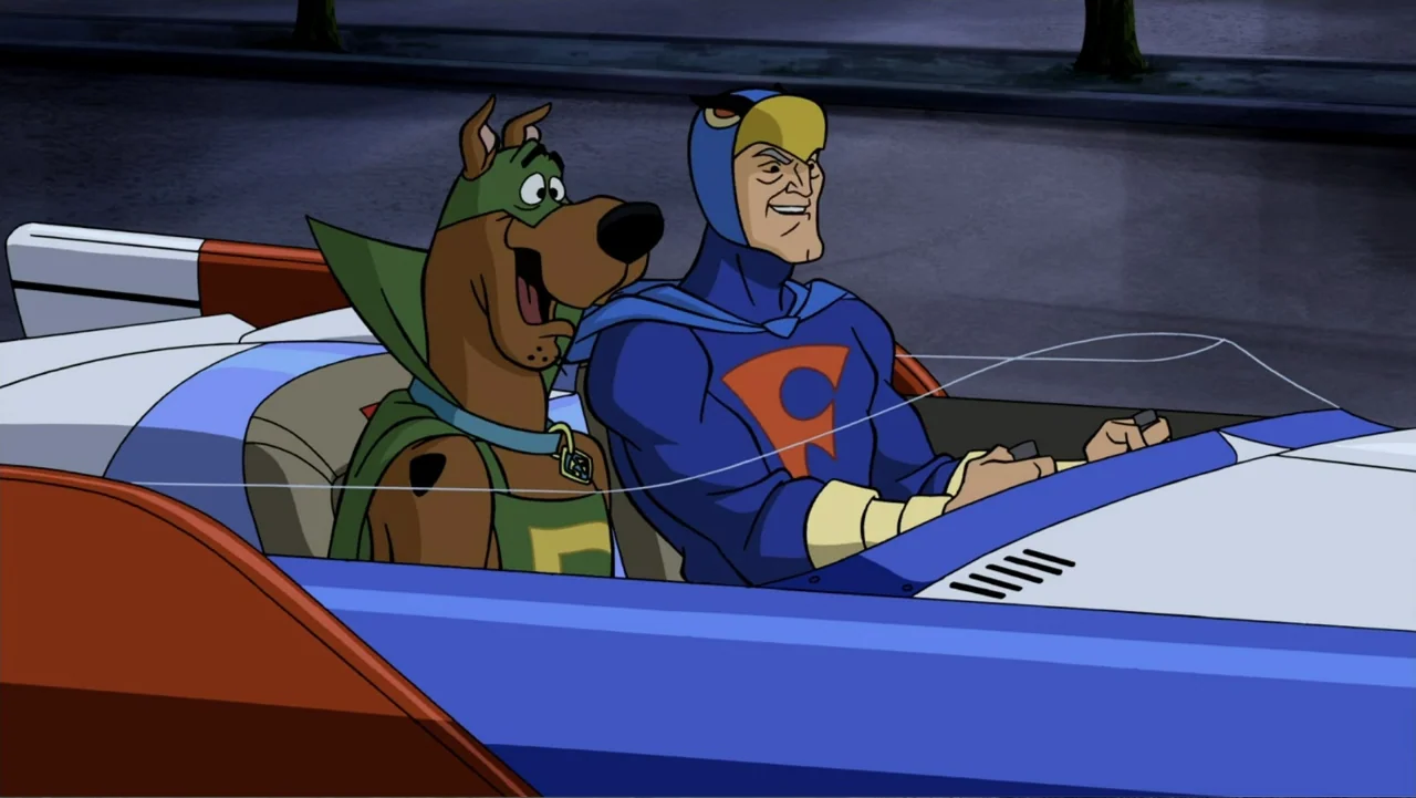 Scooby-Doo! Mask of the Blue Falcon (2012) movie still: medium — A brown dog in a green cape and a man in a blue superhero costume sit in a vehicle…