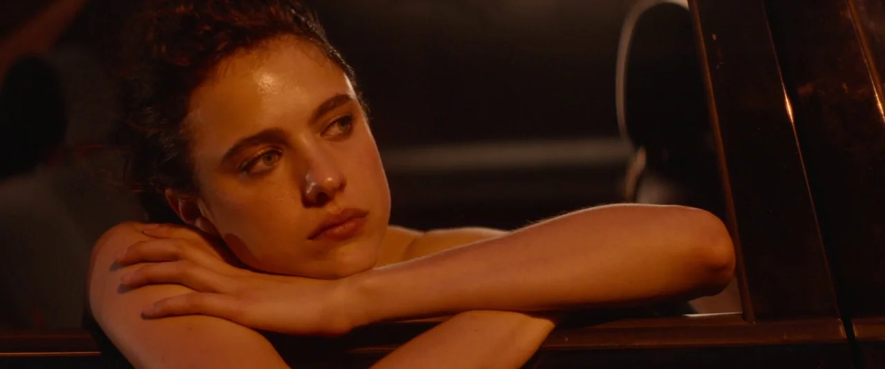 Stars At Noon (2022) movie still: closeup — A woman rests her chin on her crossed arms at night outside a vehicle. The scene is illuminated by warm…