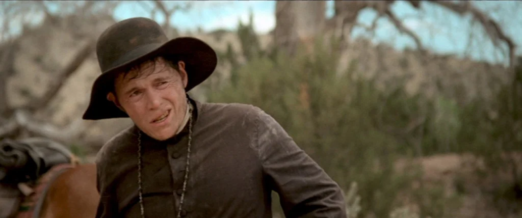 In A Valley of Violence (2016) movie still: medium — An arid desert landscape features dry shrubs and pale, parched earth under bright daylight. A…