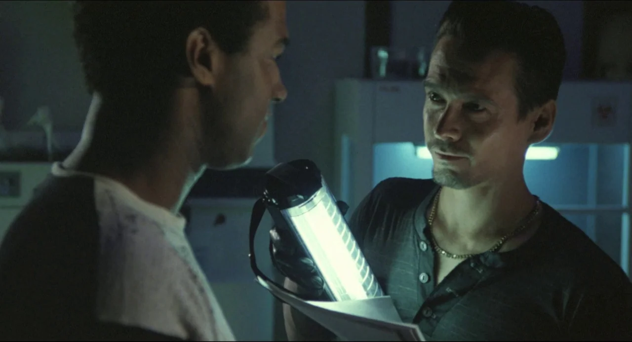 Godzilla vs. Biollante (1989) movie still: medium — Two men stand close together in a dimly lit, industrial-looking medical facility or laboratory.…