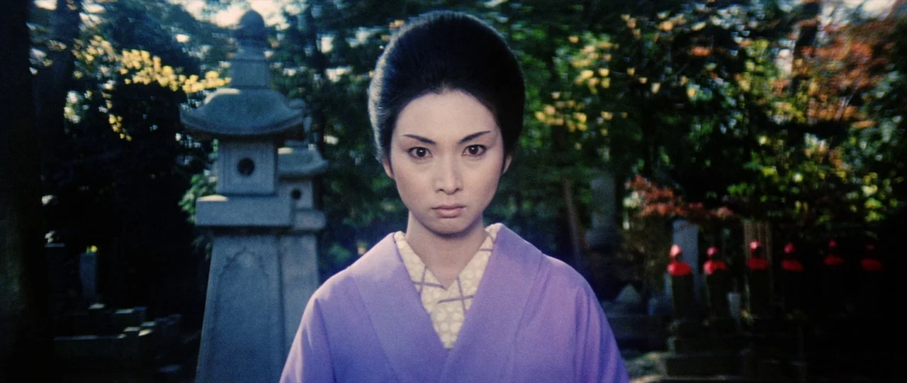 Lady Snowblood (1973) movie still: medium — A Japanese cemetery features stone lanterns and small statues among lush trees. A woman in a purple…