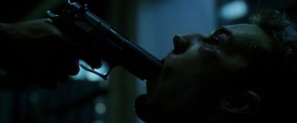 Fight Club (1999) movie still: closeup — A dark industrial environment with minimal light reflecting off metallic surfaces. A handgun is held in a…