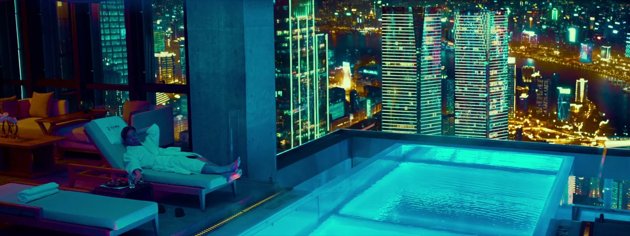 Under The Light (2023) movie still: wide — A luxury hotel suite interior features a private infinity pool overlooking a sprawling city. A man in a…