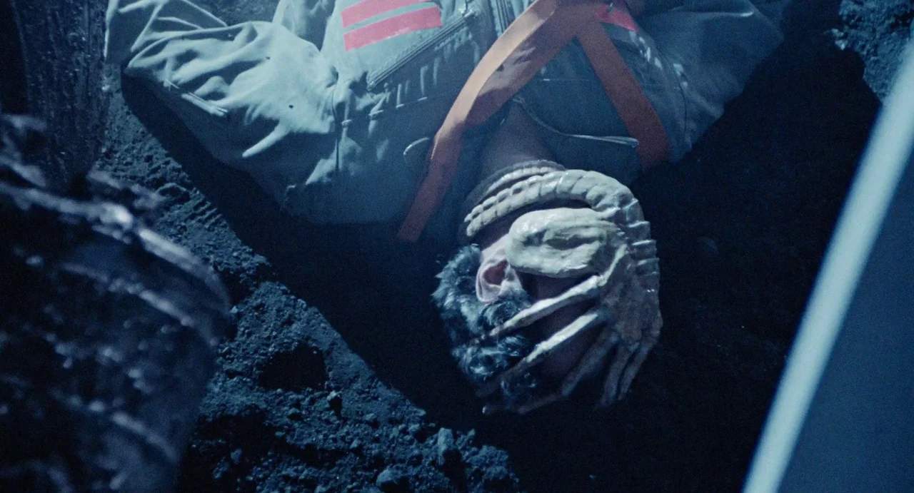Aliens (1986) movie still: medium — An uneven dark dirt surface serves as the ground for a prone figure. A light-colored creature with finger-like…