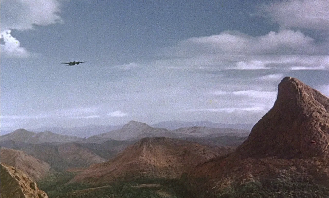 The Purple Plain (1954) movie still: establishing — An expansive mountain range under a cloudy sky features a prominent jagged peak. A small…