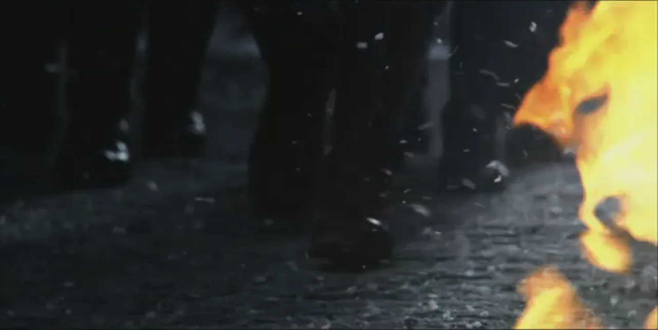 Exorcist: The Beginning (2004) movie still: closeup — Wet cobblestone ground is illuminated by bright flames from the right side. Several pairs of…