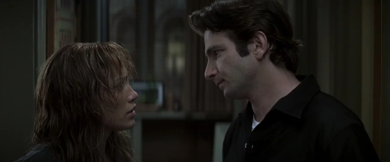 Enough (2002) movie still: medium — A dimly lit indoor corridor with dark walls and subtle architectural details in the background. A woman with wet…