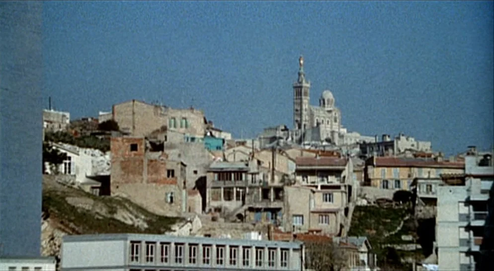 The French Connection (1971) movie still: establishing — A dense urban hillside is covered in weathered multi-story houses and brick buildings. The…