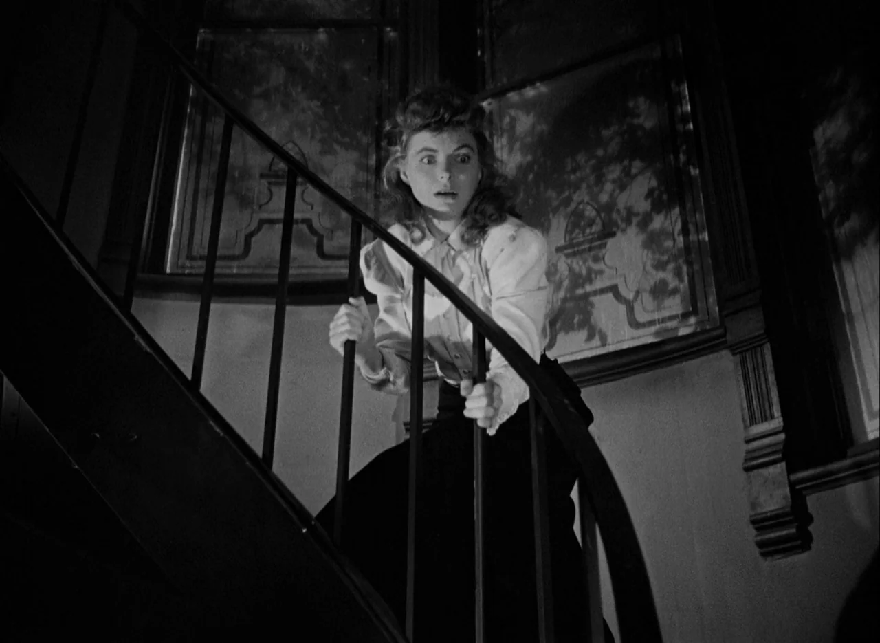 The Spiral Staircase (1946) movie still: medium — An interior staircase features dark iron railings against shadowed walls with patterned wallpaper.…