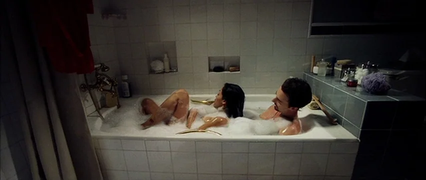 25th Hour (2002) movie still: medium — A tiled bathroom features a large porcelain tub filled with thick white soap bubbles. A man and a woman are…