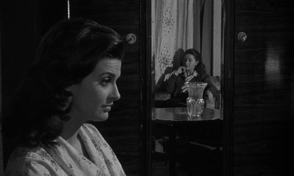 Léon Morin, Priest (1961) movie still: medium — A dark indoor setting features a woman in the foreground and another reflected in a mirror. A small…