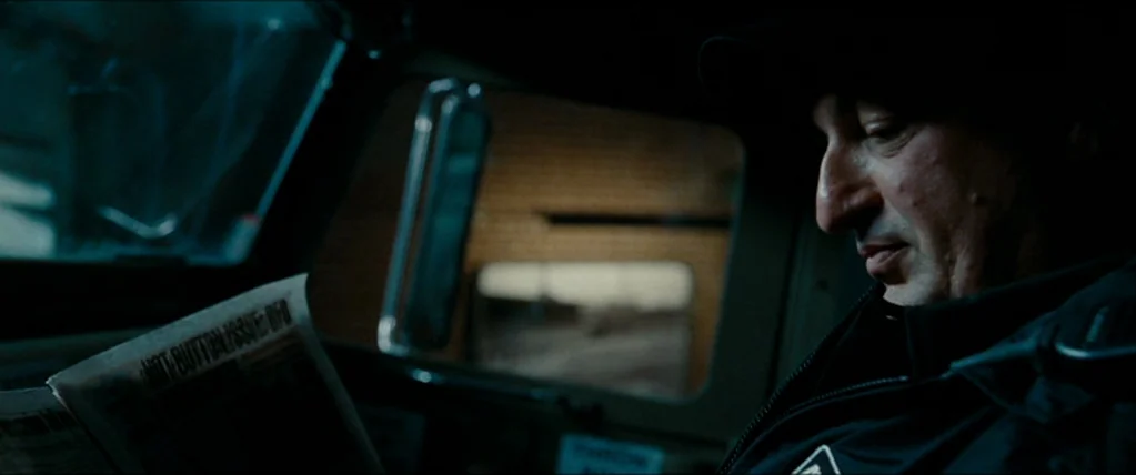 The Town (2010) movie still: closeup — The interior of a truck cab with a view through a side window. A man in a dark jacket sits in the driver seat…