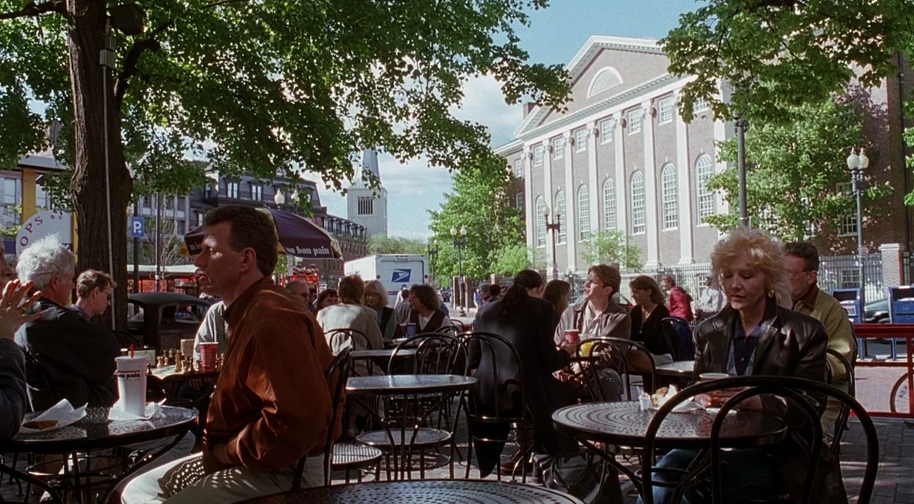 Good Will Hunting (1997) movie still: wide — A crowded outdoor cafe sits in front of a large brick academic building. People sit at circular metal…