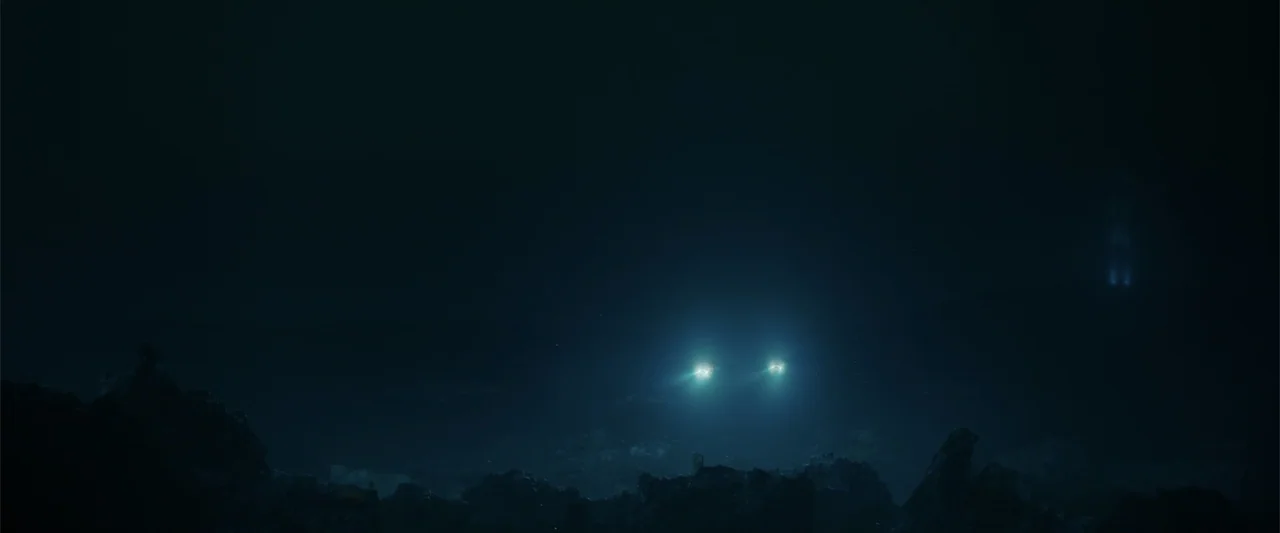 Meg 2: The Trench (2023) movie still: establishing — A vast, pitch-black underwater environment features dark rocky formations across the bottom of…
