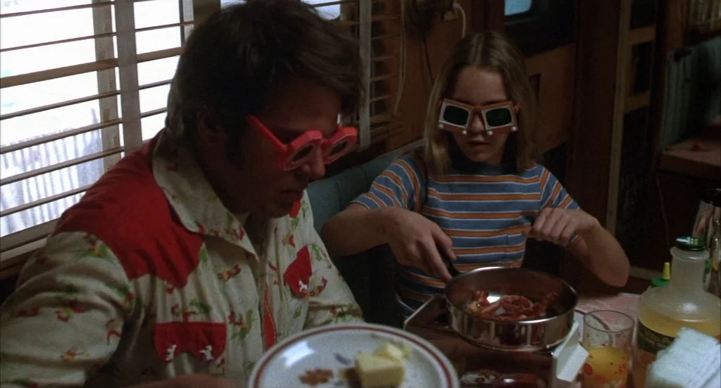 Melvin & Howard (1980) movie still: medium — A cramped interior with wood-paneled walls and slatted window blinds letting in daylight. A man and a…